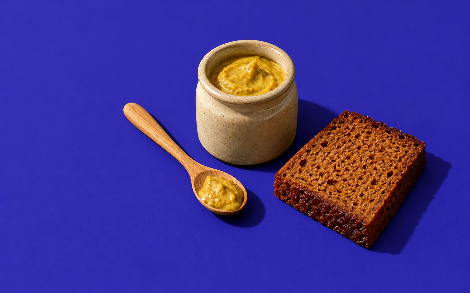 Pot de moutarde en grès, cuillère en bois et tranche de pain d'épices