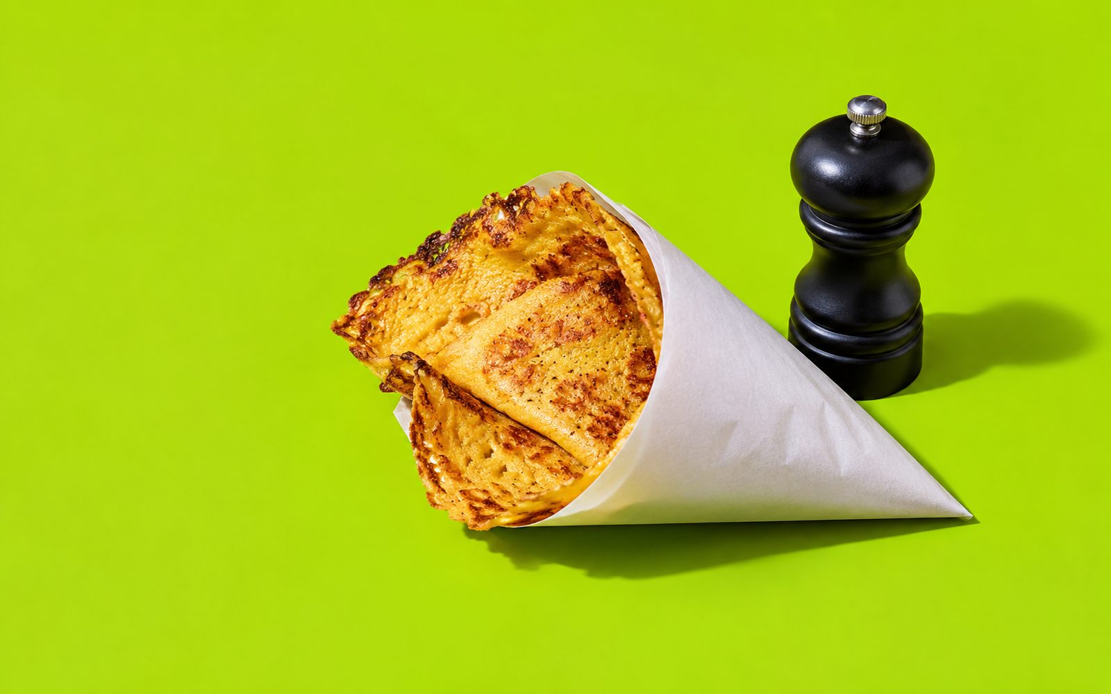 Part de socca dans un cornet de papier et moulin à poivre